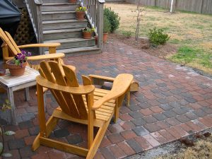 Two wooden chairs on the patio of a home, overseeing the backyard.