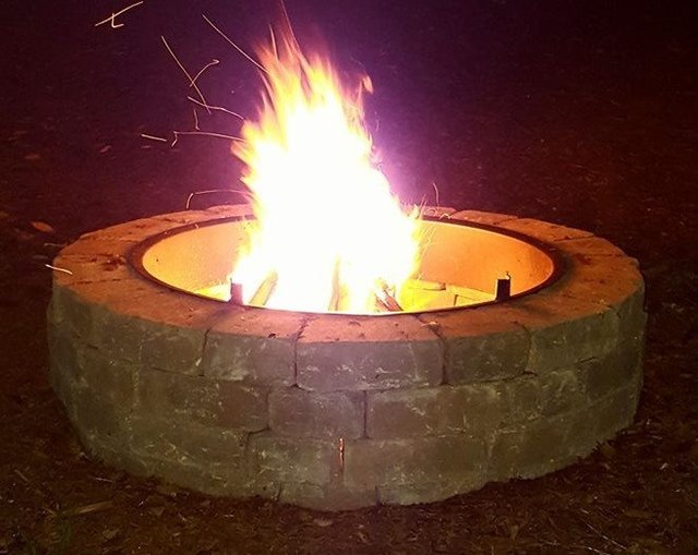 Round stone fire pit with fire at night.