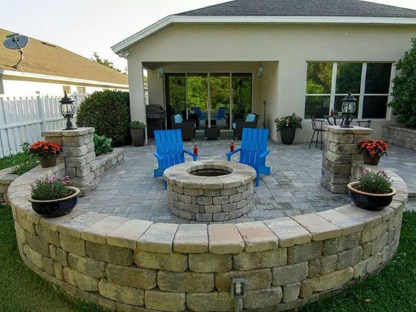 Backyard stone fire pit with two blue chairs and flower decor.