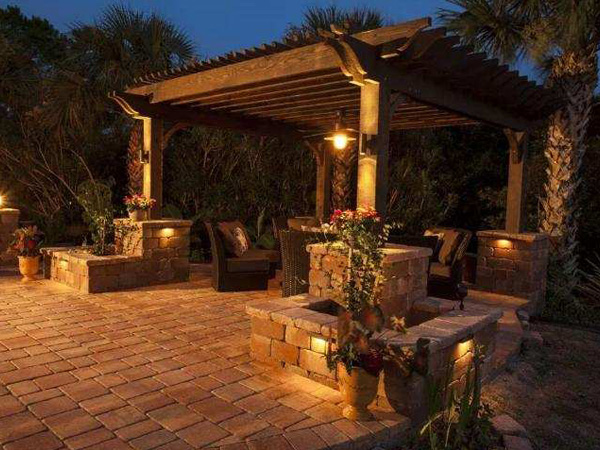 Dark evening view of a deck with pergola, decorated with outdoor furniture and accent lighting.