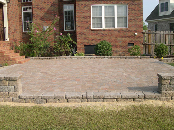 Retaining wall separating a brick paved patio and the grass in the backyard of a house.