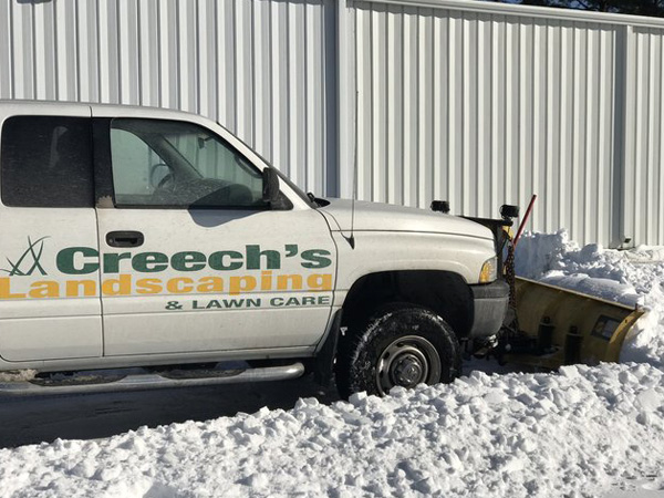 Truck plowing snow and clearing the driveway of a commercial establishment.